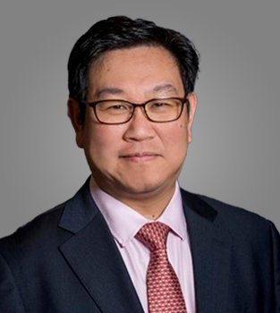 Professional portrait of an Asian man in a suit and glasses, smiling against a neutral background.