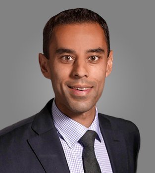 Professional headshot of a man in a suit and tie with a gray background.