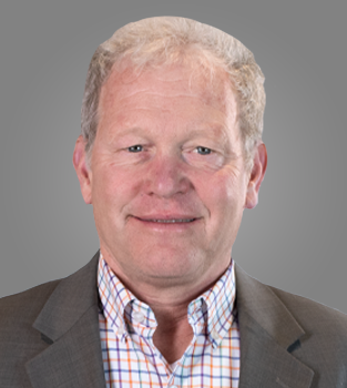 Headshot of a middle-aged man with gray hair, wearing a brown suit jacket and a checkered shirt, against a gray background.